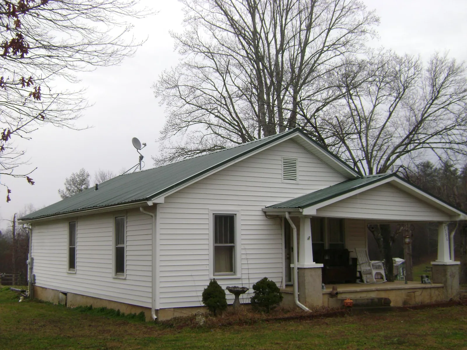 Green metal roof on a white bungalow with a side porch in Burlington